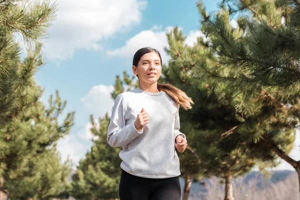 Egészséges életmód. vidám vonzó nő fut a parkban fenyőfák reggel — Stock Fotó
