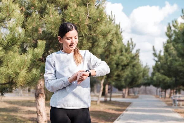 Egészséges életmód. vidám vonzó nő, aki reggel ellenőrzi a fitneszsávra vonatkozó statisztikáját a parkban — Stock Fotó