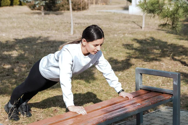 Egészséges életmód. vidám vonzó nő fekvőtámaszt csinál a padon a parkban reggel — Stock Fotó