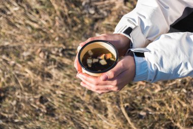 Metal yürüyüş kupasını bitki çayıyla tutan kadın elleri.