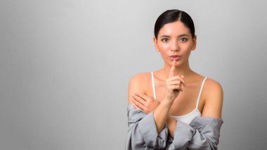 Gri gömlekli, çıplak omuzlu, muhteşem şehvetli esmer. Telif alanı geniş gri bir arka plana karşı sessiz bir jest fısıldıyor..