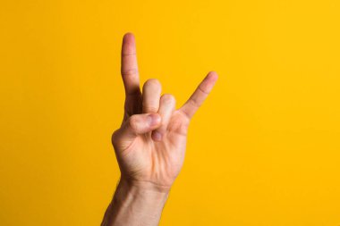 Salla gitsin. Erkek eli, sarı arka planda dramatik gölgeli kaya işareti gösteriyor.