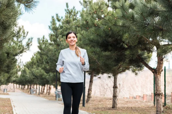 Веселая женщина в серой майке наслаждается утренней пробежкой в парке с соснами. свежий здоровый воздух — стоковое фото