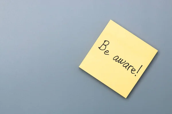 be aware on yellow sticky note over a grey background. april fools day.