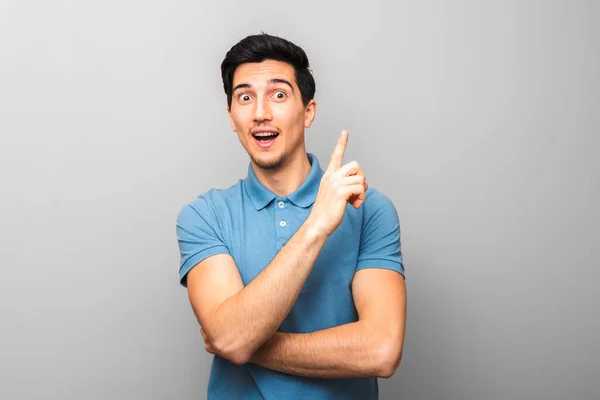 Handsome man in blue shirt got an amazing idea smiles and gestures with his finger. studio shoot against grey background. evrica — Stock Photo, Image
