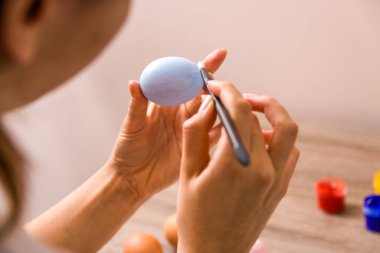 Paskalya havası. Kapatın genç kadın elleri paskalya yumurtalarını fırçayla boyuyor ve evde ahşap masanın üzerine pastel renkte balıklar çiziyor..