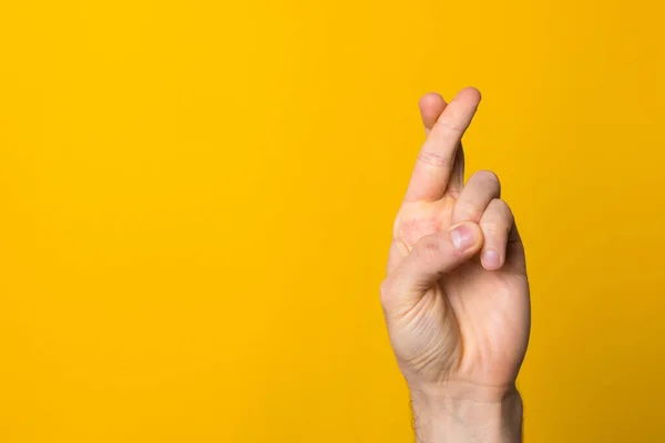 fingers crossed hope sign. close up man hand symbolising faith against yellow background
