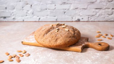 Çavdar unundan taze ev yapımı sağlıklı ekmek. Parlak mutfakta, mermer tezgahta, ahşap kırsal kesim tahtasında kabak tohumları var..