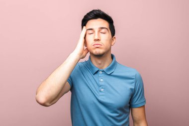 Coronavirus salgını sadece kötü haber. Mavi gömlekli, yorgun ve başı ağrıyan bir adam elini şakağının üzerine koyup pembe arka planda duruyor.