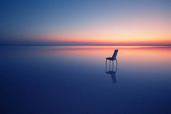 Chair among smooth water of lake at sunset