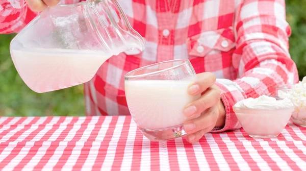 Woman pours milk from jug into glass — Stock Photo, Image