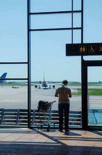 空港を眺めながら窓の前に荷物を抱えた男 — ストック写真