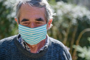 75 yaşında, tıbbi maske takmış yaşlı bir adamın portresi. Yaşlılar için koronavirüs tehlikesi kavramı.