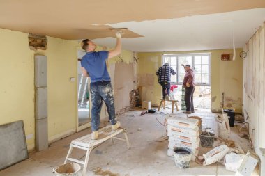 BUCKINGHAM, İngiltere - 14 Mart 2016. Müteahhitlerden oluşan bir ekip, yeni bir tavanı sıvayarak evin içini yenilemeye çalışıyor.