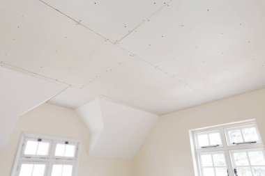 New gypsum plasterboard ceiling in room of an old house interior renovation, UK clipart