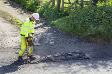 BUCKINGHAM, İngiltere - Mayıs 03, 2018. Yüksek görüşlü giysiler giyen yol işçisi hasarlı yoldaki çukurları onarıyor.