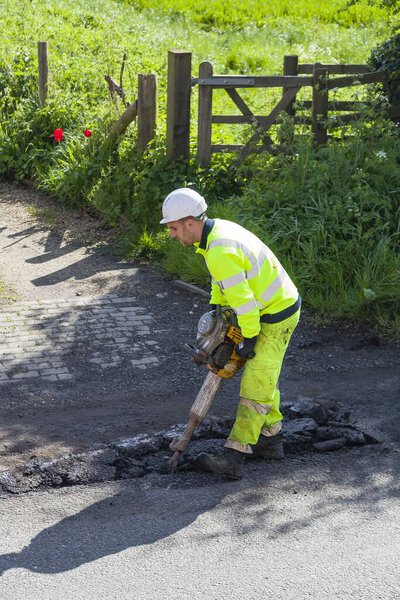 BUCKINGHAM, UK - May 03, 2018. Man wearing high visibility clothing repairing potholes in damaged road surface