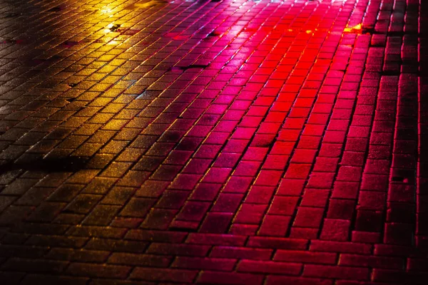 Reflejo de luces de colores en el pavimento por la noche. brillo de neón empedrado — Foto de Stock