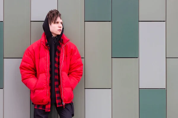 Trendy guy standing at the wall in a red jacket and looking to the side — Stock Photo, Image