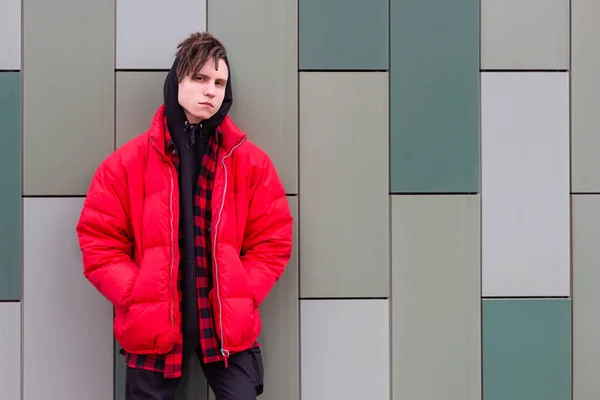 Trendig kille står vid väggen i en röd jacka och tittar på kameran — Stockfoto