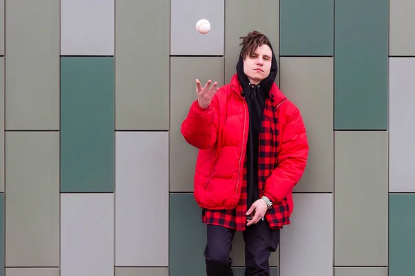 Trendig kille står vid väggen och kastar upp en boll — Stockfoto
