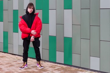 Kırmızı ceketli adam renkli duvarın yanında poz veriyor.