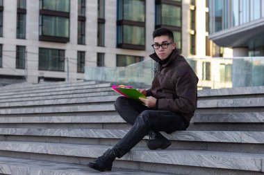 Üniversitenin basamaklarında oturan genç Asyalı erkek öğrenci kitap okuyup şöyle düşündü: