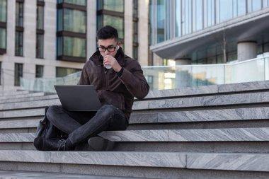 Genç Asyalı erkek programcı dışarıda dizüstü bilgisayarla çalışıyor. 