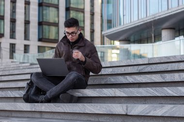 Genç Asyalı erkek programcı dışarıda dizüstü bilgisayarla çalışıyor.