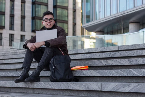 young successful Asian student programmer sit on the steps of the office laptop