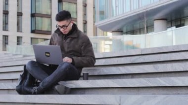 Genç Asyalı erkek programcı dışarıda dizüstü bilgisayarla çalışıyor.