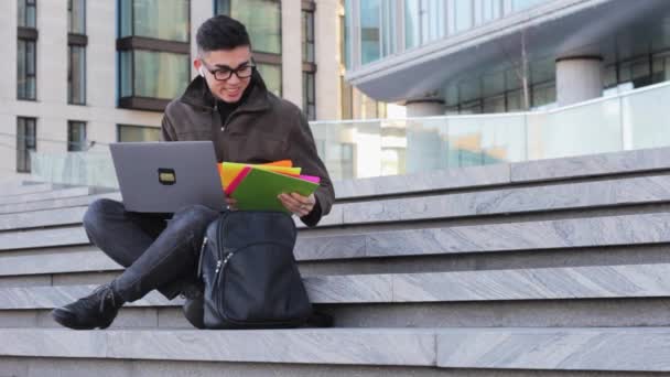 若い幸せなアジア人の学生がラップトップでステップに座って新しい仕事を得る — ストック動画