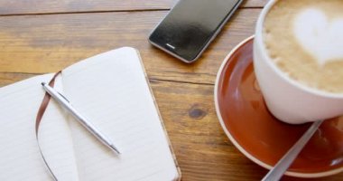 Kalp şeklinde köpük sanat günlüğü ve 4k masada cep telefonu ile sütlü sıcak kahve fincan