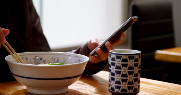 レストラン で携帯電話を使用しながら麺を持つ女性の中間セクション — ストック動画
