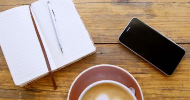 Kalp şeklinde köpük sanat günlüğü ve 4k masada cep telefonu ile sütlü sıcak kahve fincan