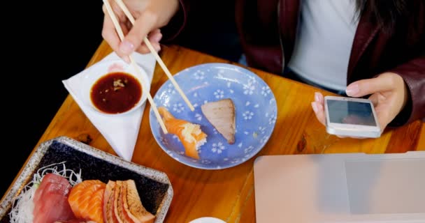 Mujer Joven Tomando Sushi Mientras Usa Teléfono Móvil Restaurante — Vídeo de stock