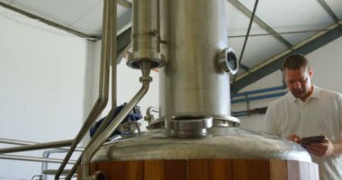 Erkek işçi fabrikada 4 k damıtma tankı incelenirken dijital tablet kullanma