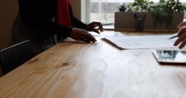 Karışık ırktan bir kadın mimar ve iki beyaz erkek mimar ofis toplantılarında bir masada mimari planlara bakıyorlar.