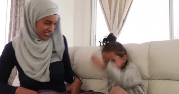 一个年轻的混血种族的母亲带着头巾和她的小女儿坐在客厅里 坐在沙发上 一起玩耍 女孩躲在毛毯下 — 图库视频影像