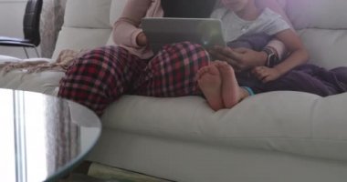 Genç melez bir annenin, genç kızıyla oturma odasında tesettüre oturup tablet bilgisayar kullanması ön planda.