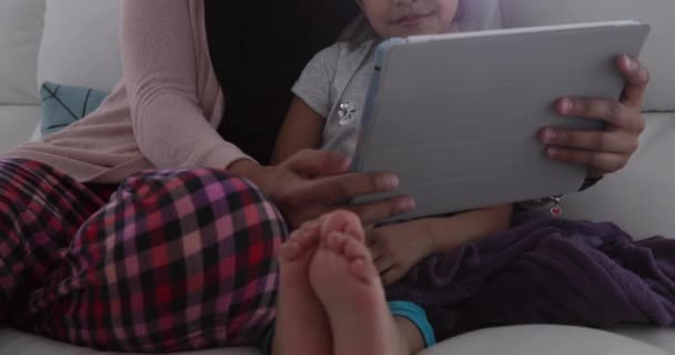 一位年轻的男女混血女子和她的小女儿坐在客厅里 坐在沙发上 用平板电脑 — 图库视频影像