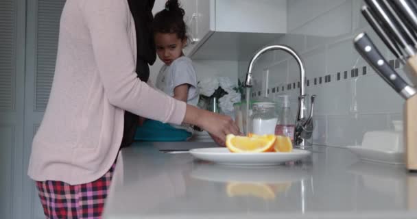 一个年轻的混血儿和她的小女儿在厨房里戴头巾 一个女人在洗澡 一个坐在工作台上的女孩的侧视图 — 图库视频影像