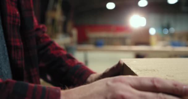一名头戴安全眼镜的白人男性木匠从一家木材店的木片上吹下锯屑的侧视图 — 图库视频影像