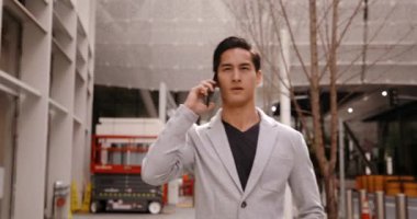 Arka planda binalar ile şehir caddesinde yürüyen akıllı telefondan konuşan genç bir ırkın ön görüntüsü.