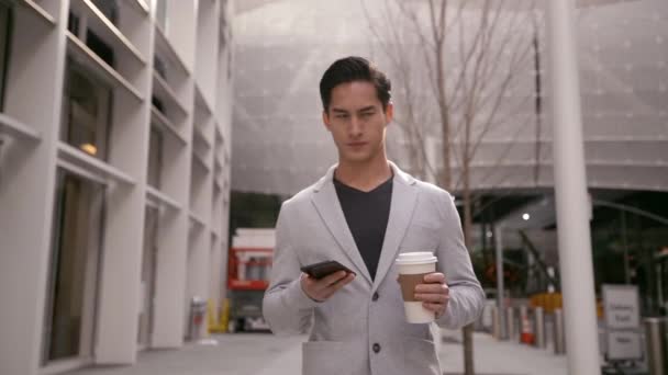 一个年轻的混血儿拿着智能手机 拿着一杯外卖的咖啡杯走在城市街道上 慢吞吞地走在镜头前 — 图库视频影像
