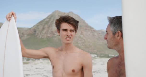 一个赤身裸体的高加索父亲和他年幼的成年儿子一起站在海滩上 一边说一边靠在冲浪板上 慢吞吞地向前看 — 图库视频影像
