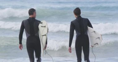 Kafkasyalı bir baba ve genç oğlunun kumsalda dalış kıyafetleri giyip birlikte sörf yapmak için sörf tahtası taşıyarak denize doğru yürürken konuştuğu arka manzara.