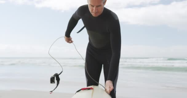 在海滩上看到一个身穿湿衣的高加索父亲 在冲浪前准备冲浪板和腿绳 身后是大海 动作缓慢 — 图库视频影像