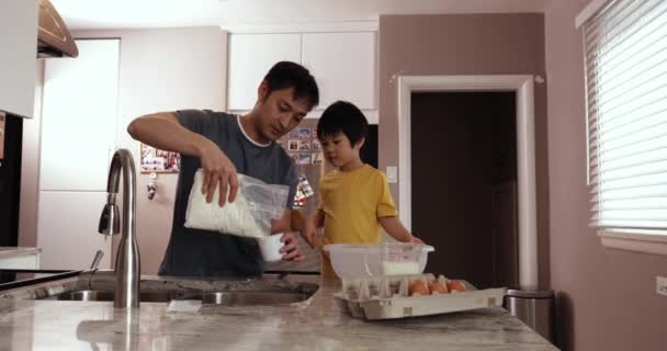 一位亚裔男子和他年幼的儿子在厨房里一起准备食物 测量配料 然后倒入一个搅拌碗的镜头 — 图库视频影像