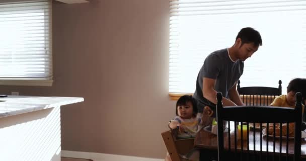一个亚裔中国男子站在餐厅的侧视图 他的小儿子和女儿坐在餐桌旁 为他们提供食物 — 图库视频影像